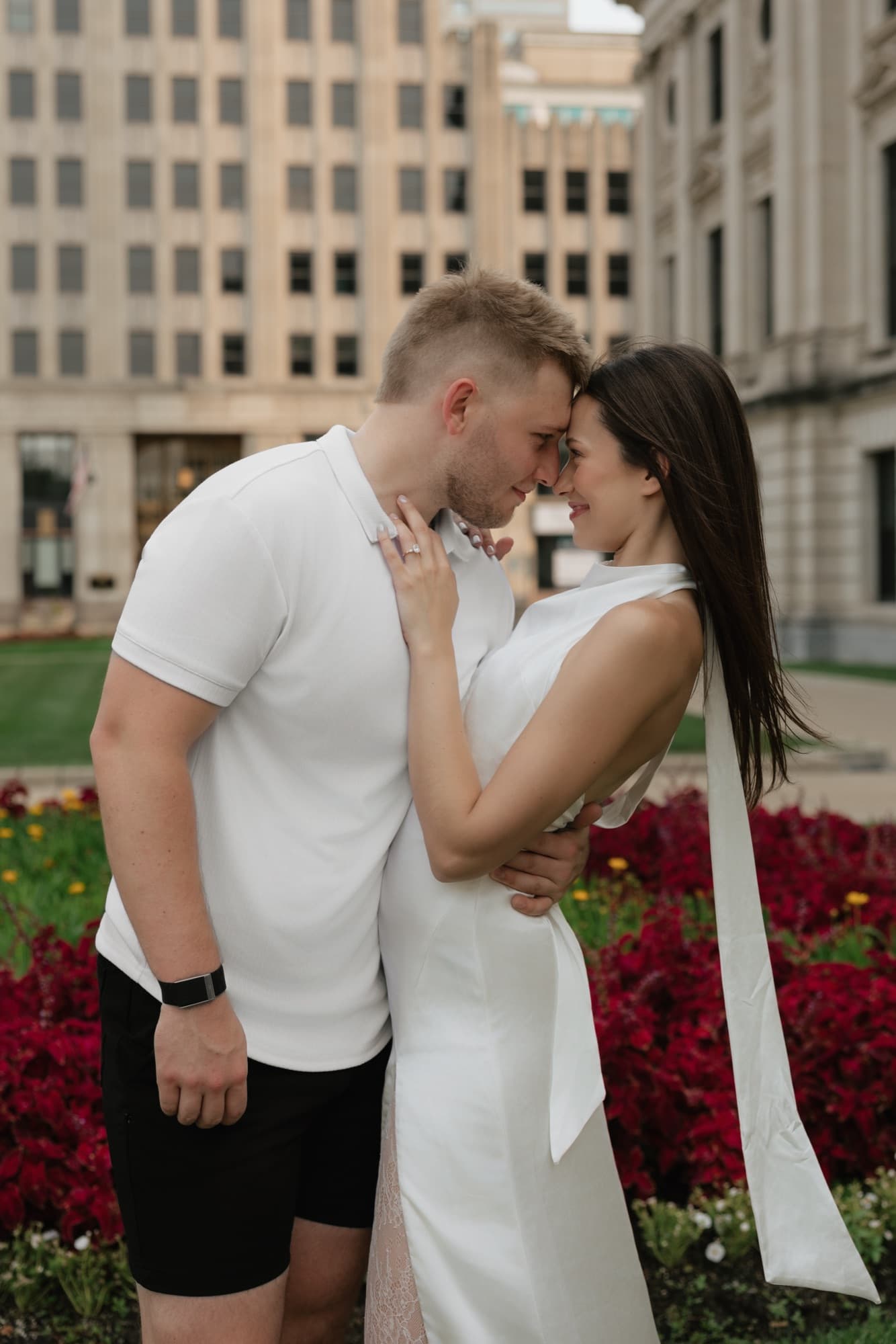 Andrew and Madeline touching foreheads among deep red flower beds downtown